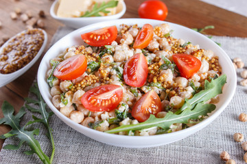 Vegetarian salad of boiled chickpeas, cheese, arugula, mustard and cherry tomatoes on brown wooden background.