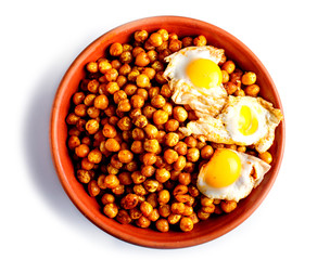 Fried chickpeas with quail eggs and spices in a clay plate isolated on white background.