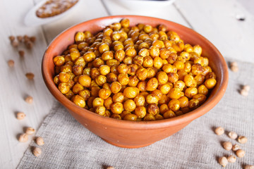Fried chickpeas with spices in a clay plate on white wooden background.