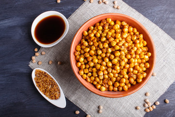 Fried chickpeas with spices in a clay plate on black wooden background.