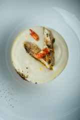 closeup fish cream soup decorated with fried pieces of fish, prawn, and spices