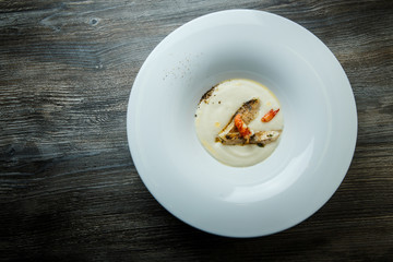 white fish cream soup decorated with fried pieces of fish, prawn, and spices