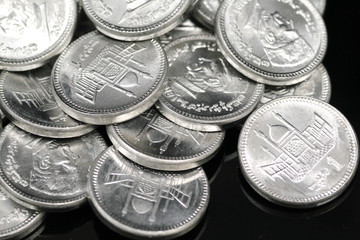 A close up image of a pile of silver Pakistani one rupee silver coins