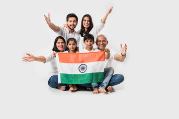 Happy Indian family holding national tricolour flag while sitting isolated over white background,...
