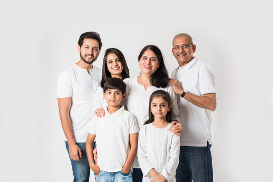 Indian Family Standing Isolated Over White Background. Senior And  Young Couple With Kids Wearing White Top And Blue Jeans. Selective Focus