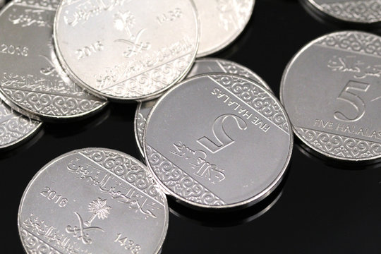 A pile of shiny new five halala coins in macro on a reflective black background