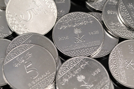 A pile of shiny new five halala coins in macro on a reflective black background