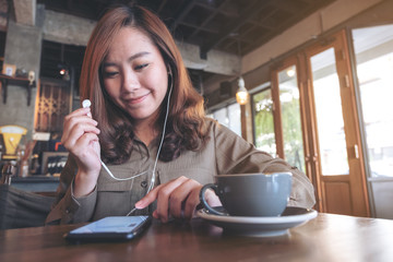 Closeup image of a beautiful asian woman holding earphones while listening to music with mobile phone  in cafe
