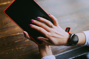 Business woman working on her coffee break in a cafe, hands of woman wearing smartwatch and holding tablet . Female hands touching screen. Close up.
