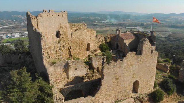The ruins of the Palafolls Castle with the Catalonia flag fluttering on a beautiful sunny day. Catalonia Spain. Aerial view travelling orbit