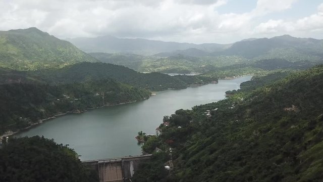 AERIAL: lifting through a valley over a dam and lake between the mountain tops of Utuado, Puerto Rico.