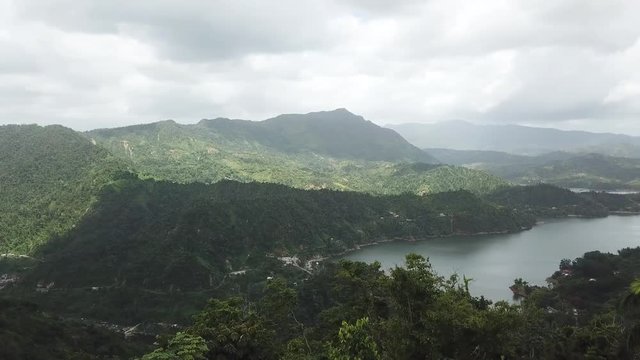 AERIAL: rotating around a large mango tree to reveal the lake in the valley between the mountain tops of Utuado, Puerto Rico.