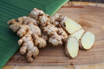 Fresh ginger root and ginger sliced on green leaf background on wood table background, healthy Asian herb concept