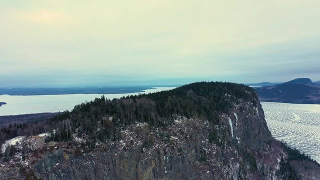 Flying backwards and down to reveal the entirety of an isolated mountain rising out of a frozen lake with a steep cliff face