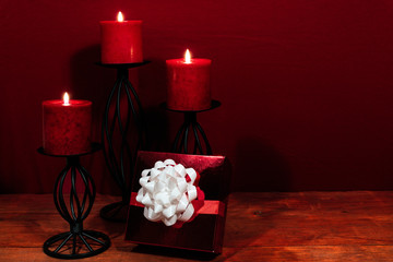 Three red candles in metal holoders and red rose, present with white bow on wooden table.