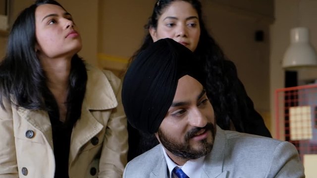 Pan left to right as a Sikh boss with turban looks disdainfully as his senior colleague and he smiles sarcastically, 