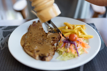 Close-up pork chop steak black pepper with men hand and black pepper sauce in white disk