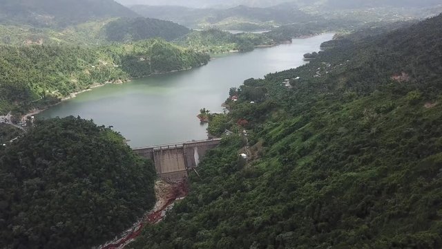 AERIAL: moving down the mountain side, towards the dam and lake, while tilting up, within the mountain tops of Utuado, Puerto Rico.