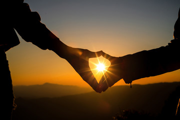 Heart shaped hands on hill at the sunset time skyline on background