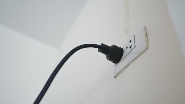 Hand plugging in an electric cord into a white plastic socket