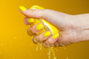 hand with yellow fingernails crushing a fresh, juicy lemon