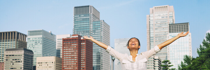 Happy asian woman with open arms up to the sky breathing fresh air in city downtown buildings...