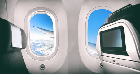 Airplane passenger seat plane interior with window view of flying aircraft wing and movie screen. - Powered by Adobe