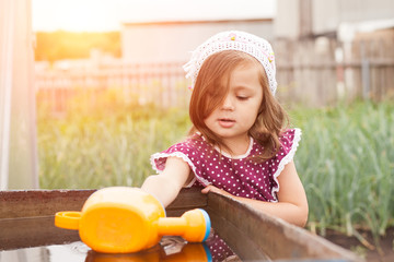 kid helps to care for the plants with a watering can in the garden