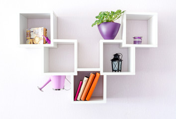 A modern white bookshelf on a white wall with a few things and a flower. Minimalism style.