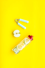 Healthy fruit water for sport, fitness. Bottle of water with lemon and cucumber near sport equipment on yellow background top view space for text