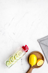 Detox infused water with slices of lemon and cucumber in bottle on white stone background top view space for text