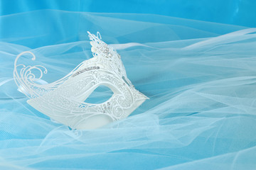 Photo of elegant and delicate white lace venetian mask over light blue silk and chiffon background