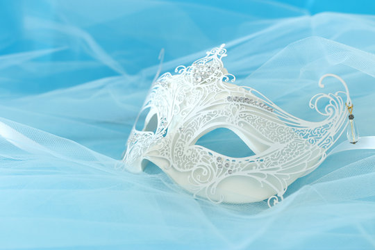 Photo of elegant and delicate white lace venetian mask over light blue silk and chiffon background
