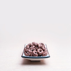 Crunchy Whole Grain Chocolate Cereals Round Oats in a Square Dish on a Wooden Table and Light Lilac Background. Healthy Organic Snack, Food, Breakfast Concept with Copy-Space