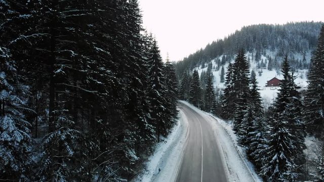Amazing view of an empty road in the beautiful winter countryside. Stunning winter landscape with forest and mountains covered with snow. Drone view.