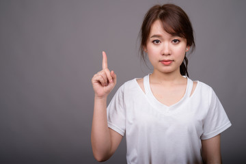 Young beautiful Asian woman against gray background