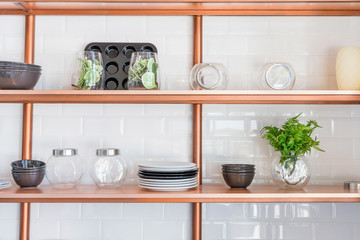 Design of a modern home kitchen in the loft-style. White wall with shelves, trays, jars, mugs, sink. In the background a wall of white brick