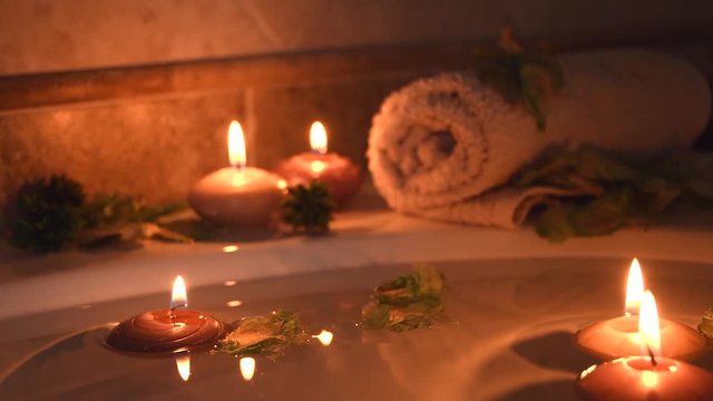 relaxing spa background with candles floating in the bath water, some green petals and a towel near the water surface