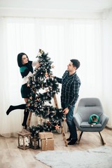 Fototapeta na wymiar Young cute couple decorate a Christmas tree on Christmas Eve