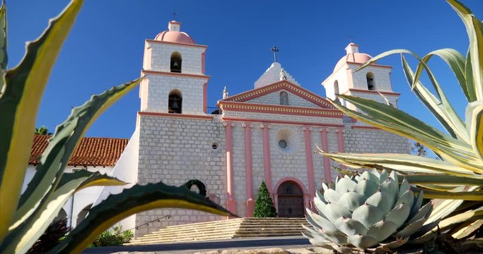 The historic Santa Barbara Spanish Catholic Mission building facade in California between succulent native plants SLIDE LEFT.