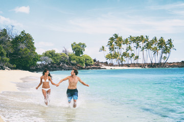 Fun beach summer vacation couple running together happy. Hawaii beach island travel holiday. Asian woman in bikini, young man.