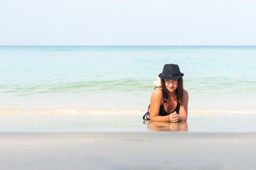 Young happy woman in swimsuit and hat is resting on the beach in Thailand.