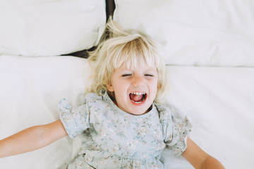 Cute little girl resting and smiling on a bed at home. Leisure. Family concept..