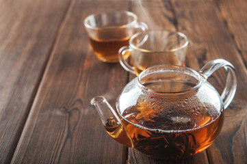 A cup of tea with fresh leaves of green and black tea on a textural dark wooden background with...