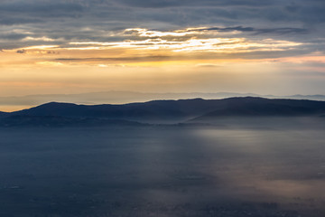 Sun rays coming down from some clouds over a valley filled by fog, illuminating part of it