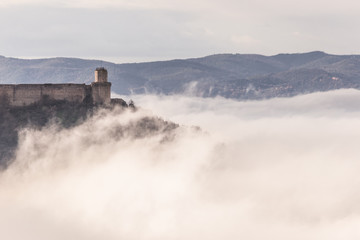 Naklejka na ściany i meble A view of Rocca Maggiore castle in Assisi (Umbria, Italy) in the middle of fog