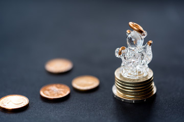 Glass angel figure over coins column on black background