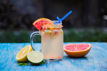 Grapefruit lemonade in pitcher of citrus around on wooden table on blue background