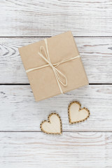 Kraft box with two wooden hearts on white wooden background.