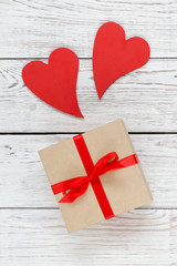 Kraft box with two red hearts on white wooden background.